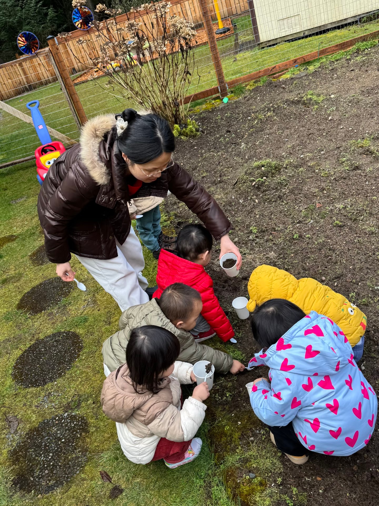 Panda Bear Childcare — adult teaching children outdoor gardening activity